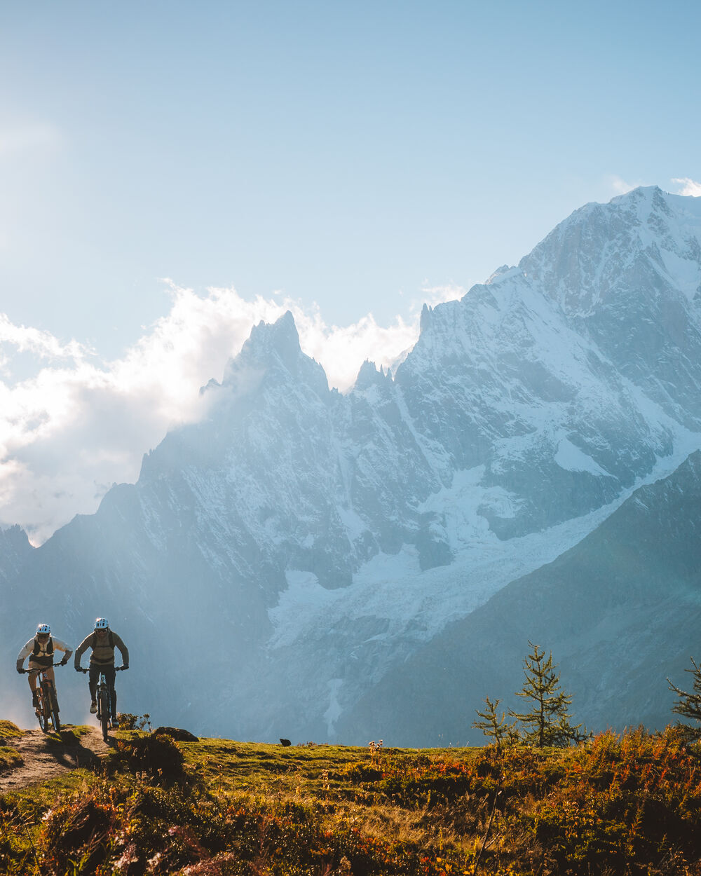 Two riders on a ridge with the Mont Blanc massif behind them